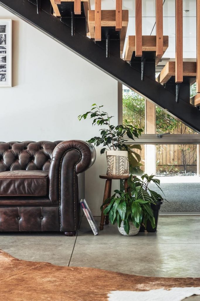 Piso de concreto usado em uma sala, com tapete de pele e sofá de couro marrom. 
